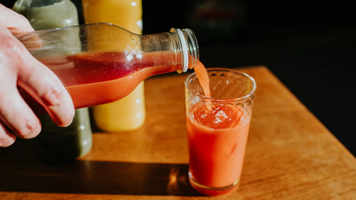 A hand filling a cup with vegetable juice