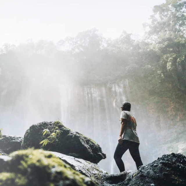 Man in the jungle looking at a waterfall