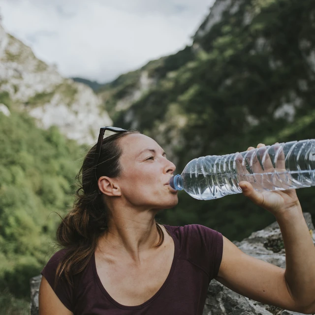 Mid adult female trekker drinking from plastic water bottle while looking away.