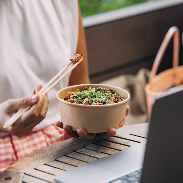 Woman using chopsticks to eat food from disposal box