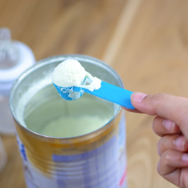 Powder milk and blue spoon on light background close-up