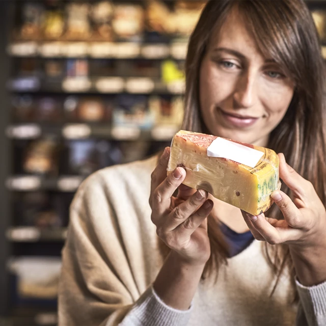 A woman in a supermarket examining a wedge of continental cheese 
