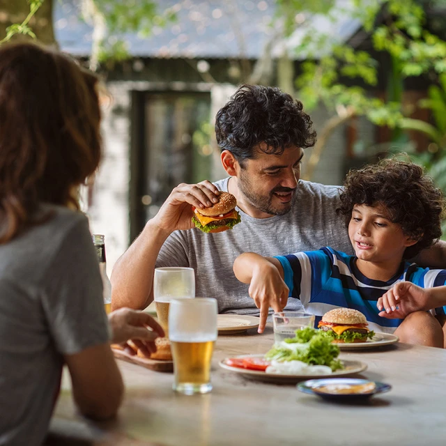 A family in the garden eating burgers with melted cheese slices.  