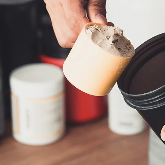 Hands holding scoop of whey protein and shaker 