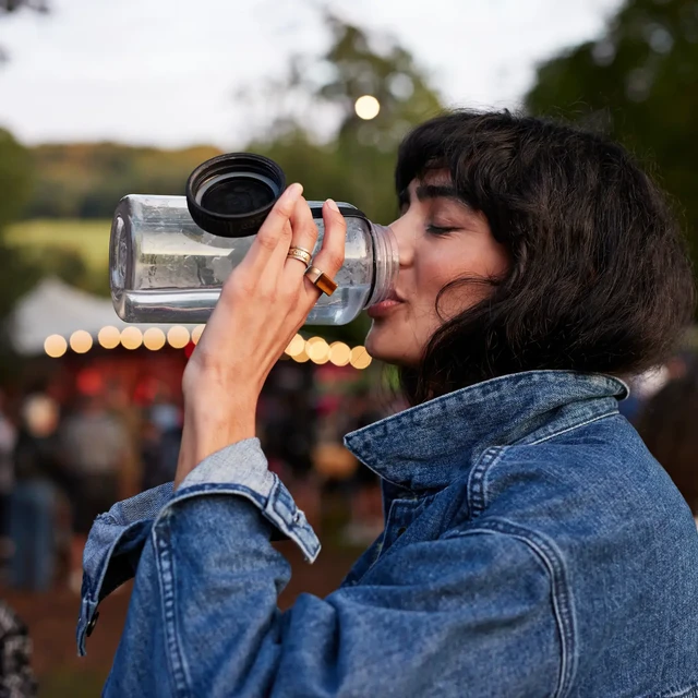 Woman with a denim jacket drinking from water bottle 
