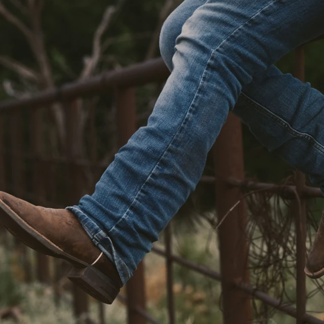 a person wearing jeans and boots sitting on a fence