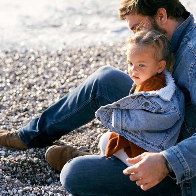 a man holding a girl wearing denim wear sitting on a beach