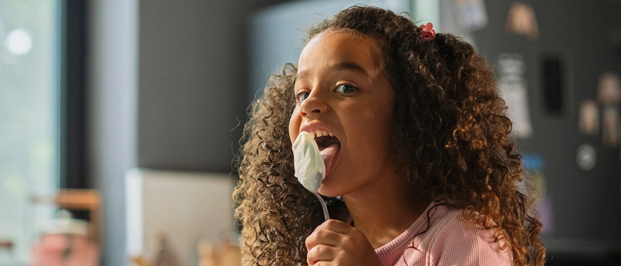 Little girl eating yogurt with a large spoon, and licking the spoon