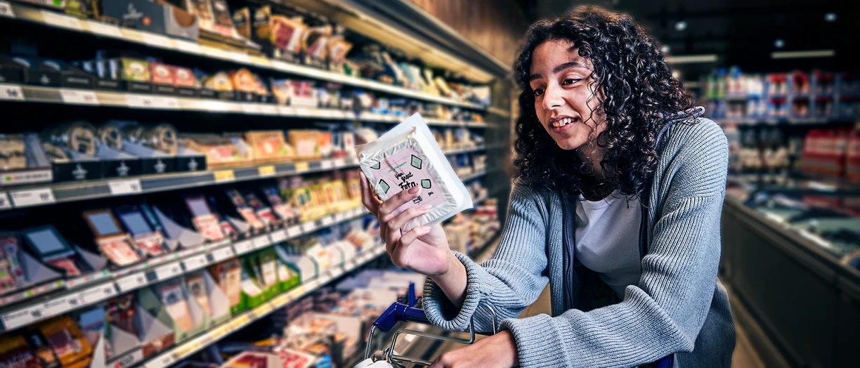 Woman with curly hair examines a package of feta cheese while shopping in a grocery store