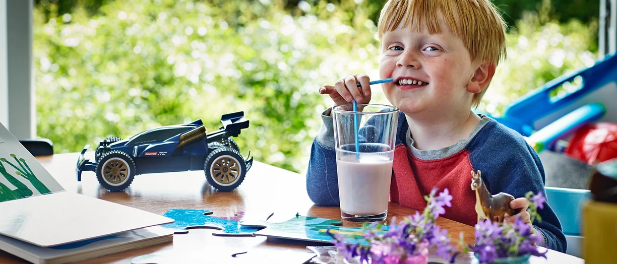 Child with red hair drinking a glass of milk at a table