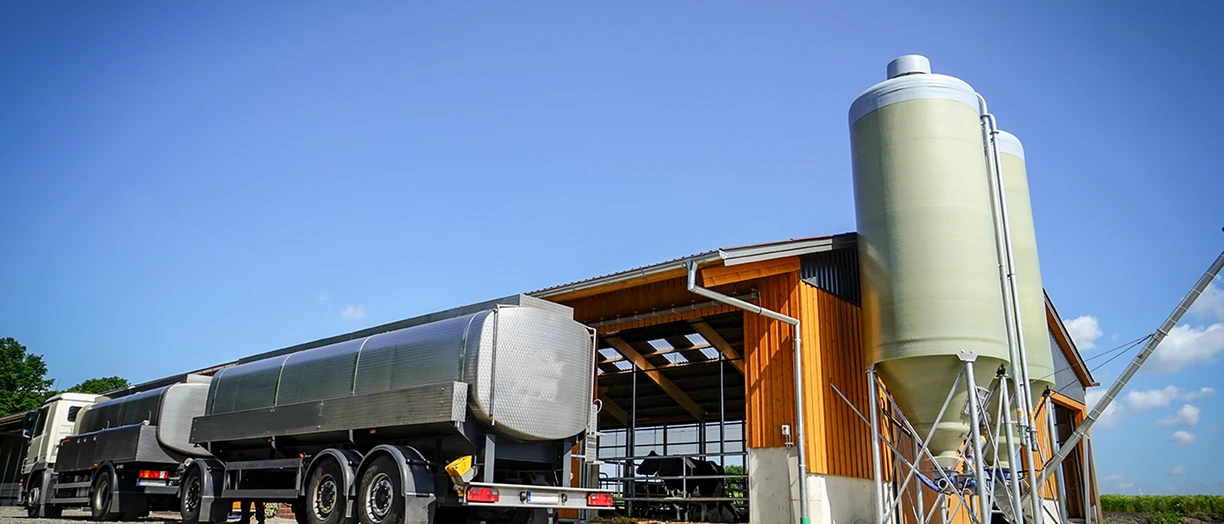Tanker truck parked by a farm building with silo