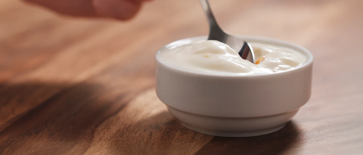 Young female hand eating peach yogurt with spoon.png
