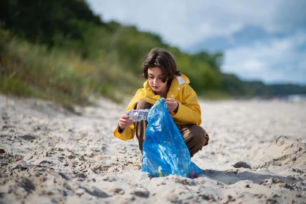 Preteen ecological girl cleaning beach from plastic waste