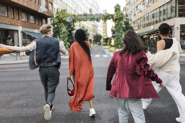 Rear view of multiracial friends crossing road while walking in city