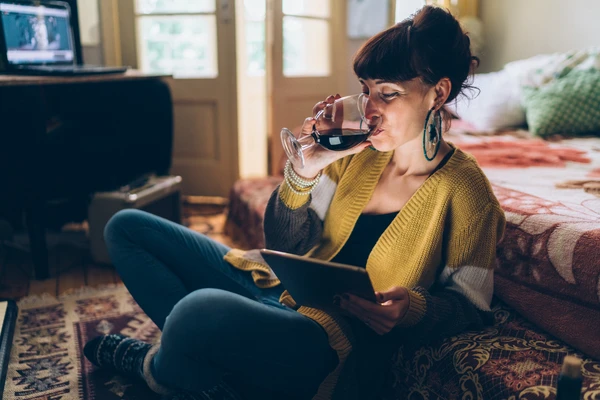 Woman_sitting_at_home_drinking_red_wine_while_looking_at_a_tablet