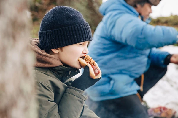 A boy sitting outside eating a hotdog