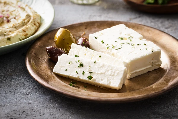 Plate with two slices of Feta cheese topped with chopped herbs, accompanied by olives. 