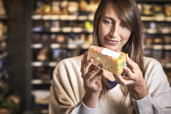 A woman in a supermarket examining a wedge of continental cheese 