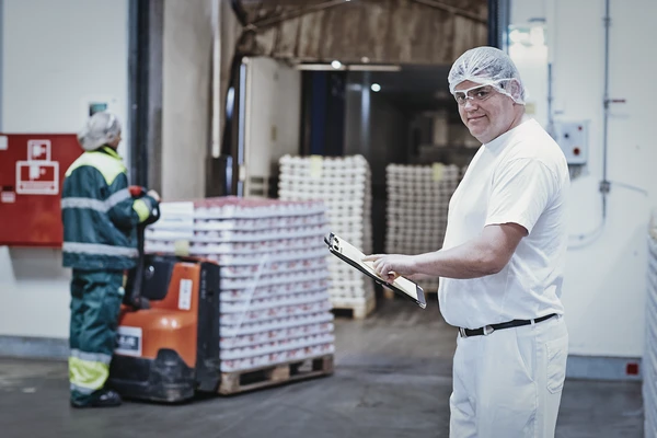 A dairy worker with a clipboard in the foreground, as in the background wooden pallets full of yogurt