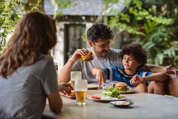 A family eating burgers in the garden. The burgers have slices of cheese melting on them. 