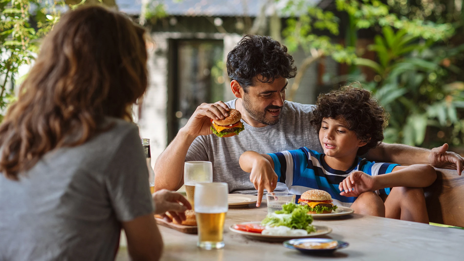 A family in the garden eating burgers with melted cheese slices.  