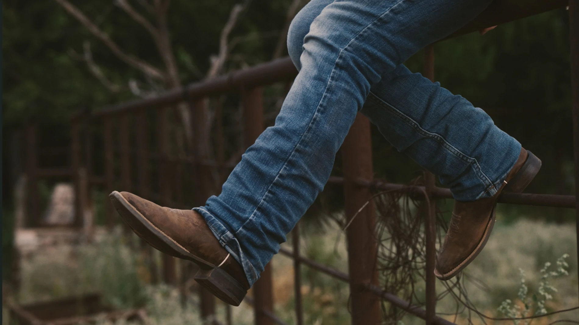 a person wearing jeans and boots sitting on a fence