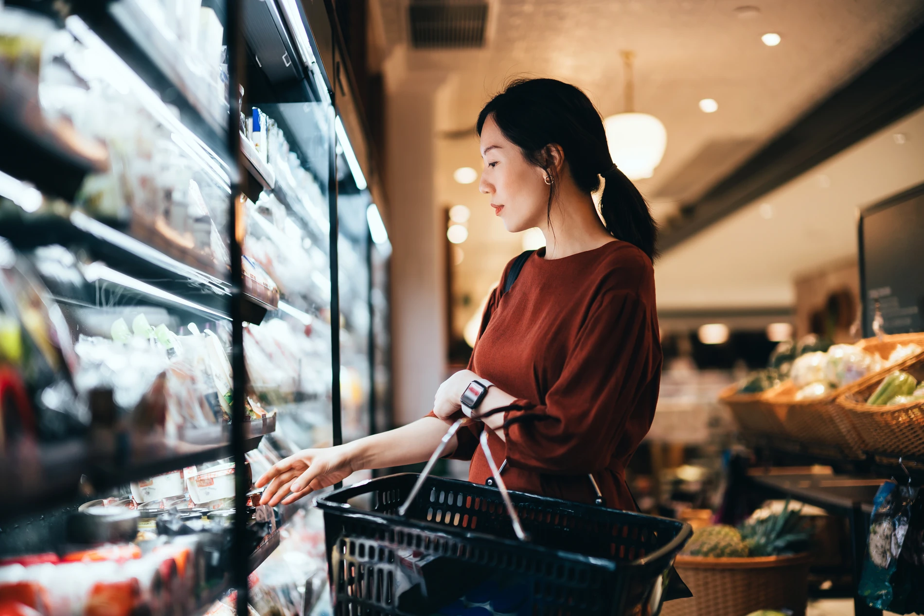 asian woman staning the the vegtables department of a supermarket