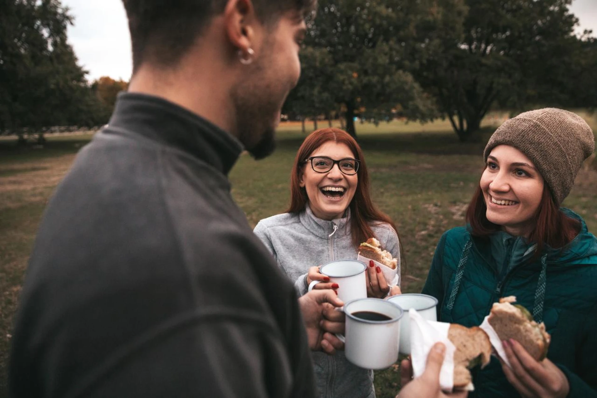People laughing and eating sandwiches in a park