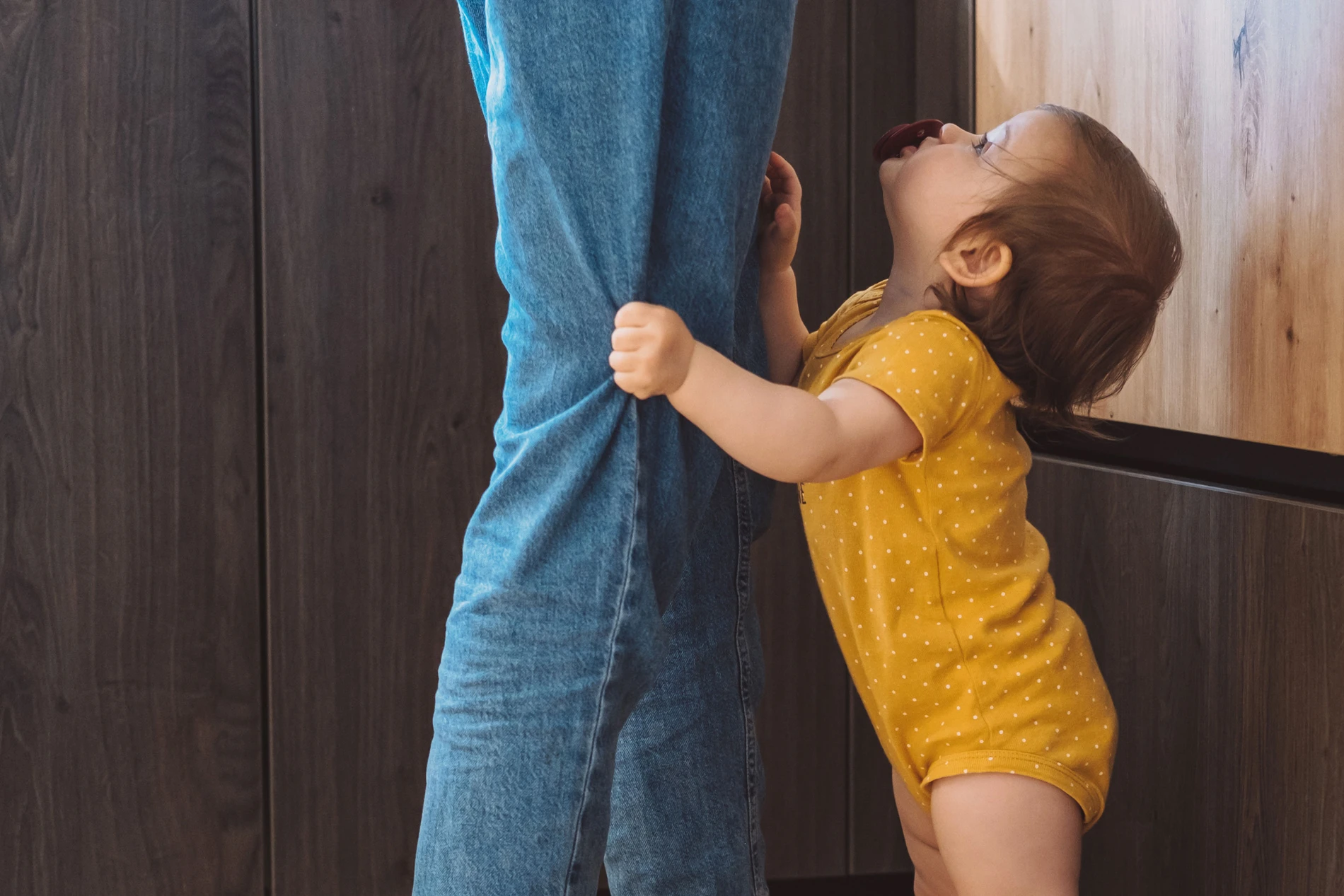 a baby holding an adult's jeans